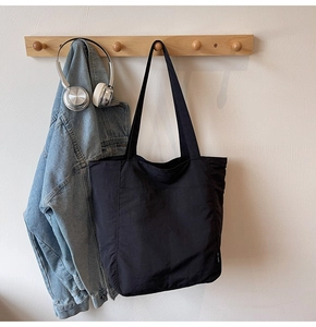 Detailed view of black nylon tote bag hanging on wooden hook in a lifestyle setting