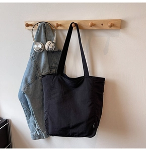 Close-up of a black minimalist tote bag on a wooden hook with stylish denim jacket