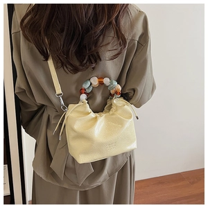 Detail view of cream bucket bag featuring pleated leather and marble bead handle