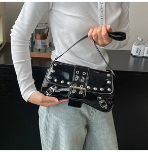 Detalle de bolso de hombro en charol negro con remaches plateados y hebilla metálica