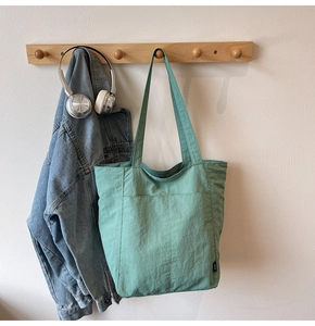 Detail of sage green tote bag with front pocket hanging on wood hook in home setting