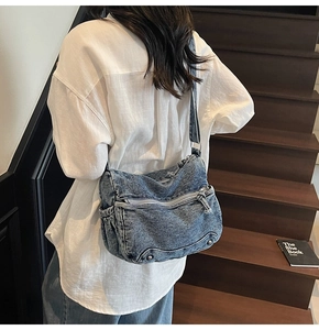 Detail of blue wash denim crossbody bag featuring multiple zipper pockets and wide strap