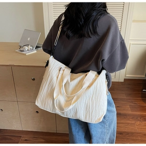 Detail shot of a white pleated canvas tote bag showing draped shape and shoulder strap