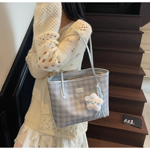 Detail view of grey plaid tote bag with silver trim and a white plush star pendant charm