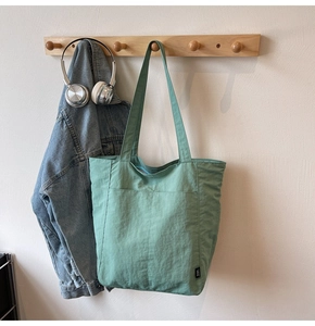Detail of mint green tote bag on wood hook with denim jacket and headphones