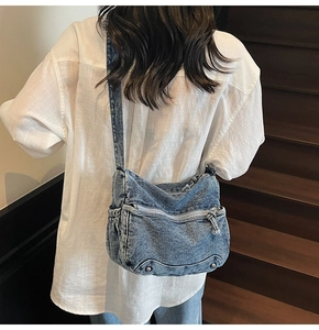 Close-up of blue washed denim crossbody bag featuring functional zipper pockets and cargo style