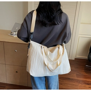 Close-up of white pleated canvas tote bag with wide straps and metal buckles on a desk