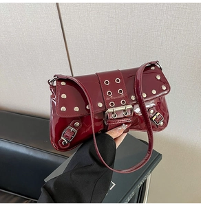Close-up of burgundy patent leather baguette bag with silver eyelets and punk metal buckles