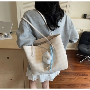 Detail view of cream checkered tote bag with plush charm on a model's shoulder