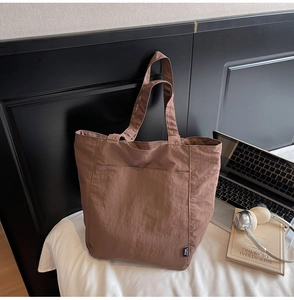 Detailed view of brown tote bag on white bed with laptop and study accessories