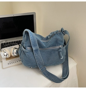 Blue denim tote bag with side zipper and fringe detail on a desk with a laptop