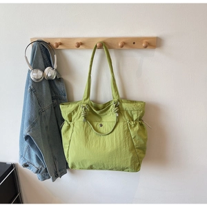 Détail du cabas en nylon vert avocat avec poche à cordon suspendu à un crochet en bois