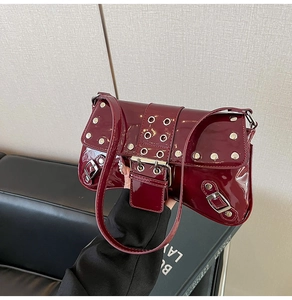 Detalle de bolso baguette en charol burdeos con tachuelas plateadas y ojales metálicos