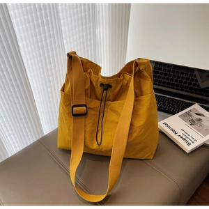Detailed view of yellow nylon shoulder bag with adjustable strap on a leather bench