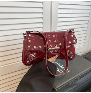 Detalle de bolso en charol burdeos con remaches plateados y ojales metálicos decorativos