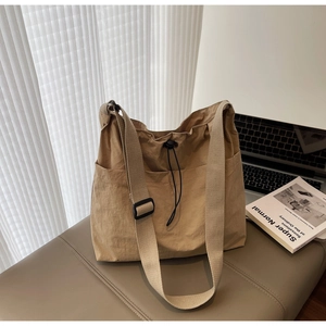 Close-up of khaki drawstring bucket bag with side pockets and wide strap on grey bench