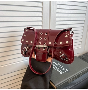 Detalle de bolso de hombro en charol rojo oscuro con tachuelas plateadas y hebilla fina