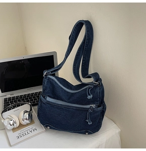 Detail of blue denim shoulder bag with multiple zippers and studs in a lifestyle setting