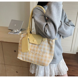 Detail of checkered tote bag featuring cartoon embroidery and a mini side pouch accessory