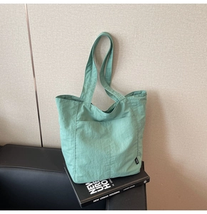 Detail of mint green nylon tote bag featuring front pocket and side woven label