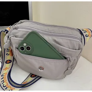Detail of light grey nylon crossbody bag showing multiple zip pockets and a phone storage