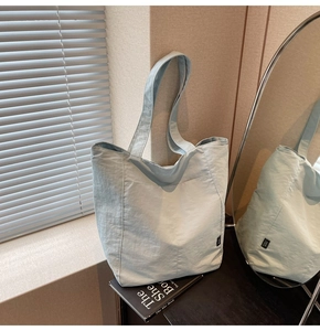 Detail of light blue tote bag with micro-wrinkle texture and side label in natural light