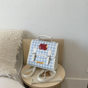 Dettaglio dello zaino a quadretti blu con ricamo a mela rossa e scritta Not Anxious