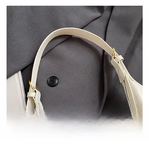 Détail du sac en cuir crème montrant une large bandoulière et une boucle dorée ajustable