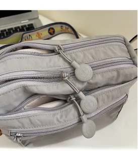 Close-up of smooth triple-zipper system on a light grey nylon crossbody storage bag