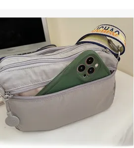 Detail of grey oxford fabric crossbody bag showing front zipper pocket for mobile phone storage