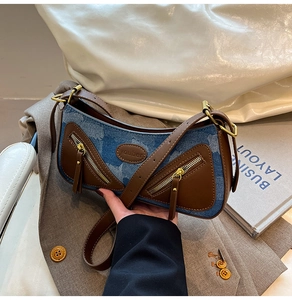 Detail of vintage denim baguette bag featuring brown leather trim and twin zip pockets