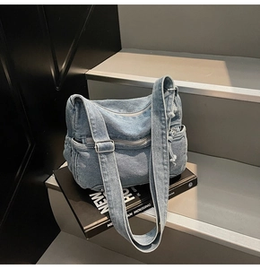 Detail view of the blue denim tote bag featuring multiple zip pockets and adjustable strap