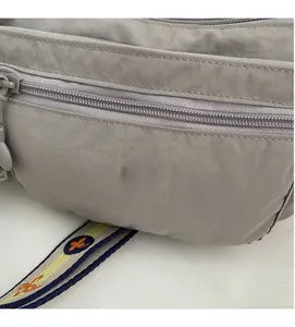 Detail of grey nylon crossbody bag showing metallic emblem and embroidered wide strap