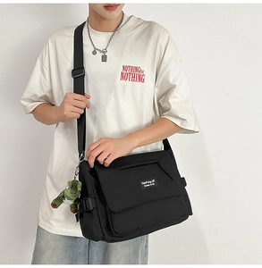 Detail of black canvas messenger bag with brand logo label and green dinosaur charm