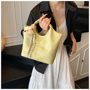 Detail of pale yellow crocodile texture handbag with plush bear charm and woven tassel