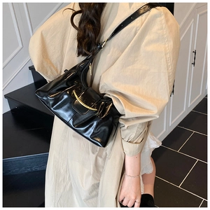 Détail du sac à bandoulière noir brillant avec boucle en métal doré sur un mannequin