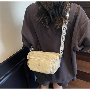Detail of beige nylon crossbody bag showing multiple zip pockets and patterned strap