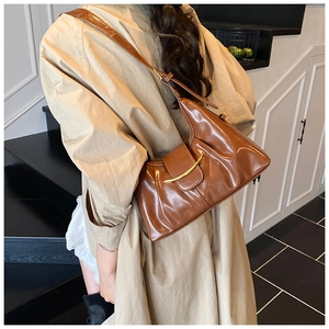 Détail d'un sac en similicuir marron caramel avec barre métallique dorée et design plissé