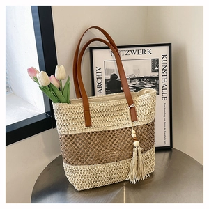 Dettaglio borsa tote in paglia intrecciata a righe con manici in pelle e nappa decorativa