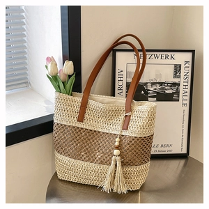 Dettaglio della borsa tote in paglia a righe con manici in pelle marrone e nappina di legno