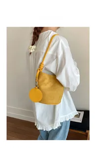 Detail view of bright yellow suede bucket bag with a round coin purse on a model