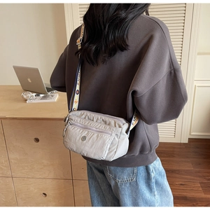 Detail of grey Oxford fabric crossbody bag with multi-zipper layers and pattern strap