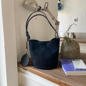 Detail view of black matte suede bucket bag on a wooden table with lifestyle decor