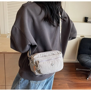 Detail view of a taupe nylon crossbody bag with multi-pocket design and wide lettered strap