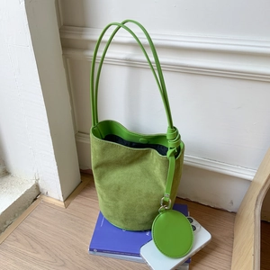 Detail view of green suede bucket bag with round coin purse and decorative knotted strap