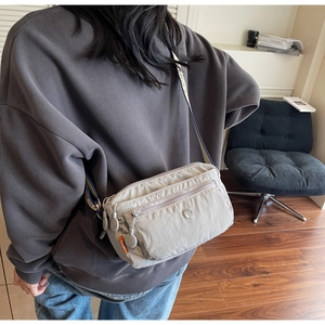 Detail of a casual nylon crossbody bag featuring multi-zipper pockets and a woven strap