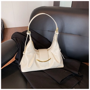 Gros plan du sac brillant crème avec boucle dorée posé sur un fauteuil en cuir noir