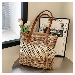 Dettaglio della borsa tote in paglia con manici in pelle marrone e dettaglio di nappa decorativa