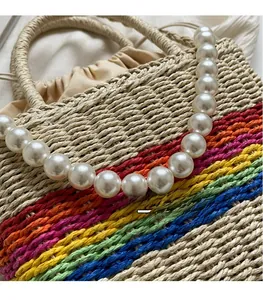 Close-up of woven straw bucket bag featuring rainbow stripes and white pearl handle