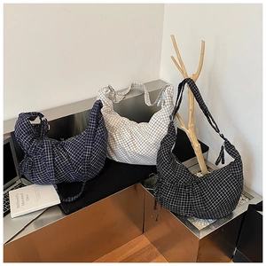 Close-up of three plaid canvas hobo bags in blue, beige, and black on a laptop desk